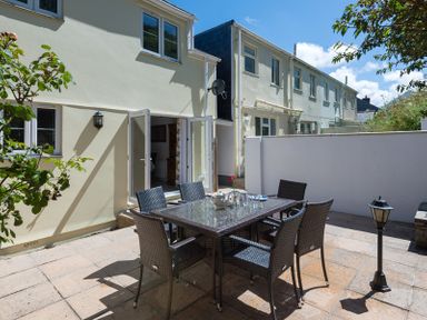 An outdoor patio area with a table and six chairs next to a cream colored building with open double doors at Stop Tide in Port Isaac