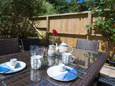 An outdoor dining table with plates cups spoons a teapot a jug and a red rose in a vase at Stop Tide in Port Isaac