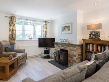 A living room with a stone fireplace a TV a grey sofa and an armchair at Stop Tide in Port Isaac