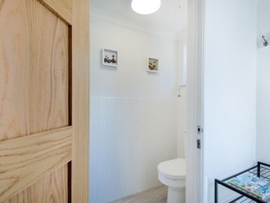 A bathroom with a toilet a wooden door two pictures on the wall and a metal rack with magazines at Stop Tide Port Isaac