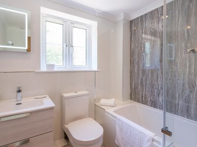 A bathroom with a sink cabinet toilet bathtub with towel and gray marble wall at Stop Tide in Port Isaac