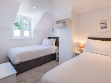 A bedroom with two single beds a window a nightstand with a lamp and a wall-mounted shelf with hangers at Stop Tide in Port Isaac