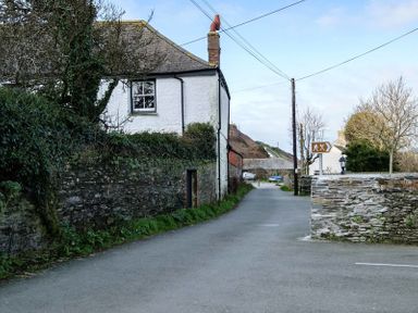 A narrow road with stone walls and a white house surrounded by trees and bushes at Stop Tide in Port Isaac