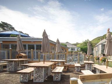 An outdoor seating area with wooden picnic tables and umbrellas at Stop Tide in Port Isaac