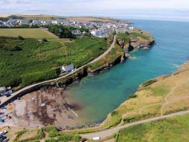 A coastal village with houses near a cove with green cliffs and a small beach at Stop Tide in Port Isaac