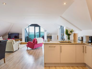 An open-plan kitchen and living room with a pink chair and beige armchairs near a TV and glass doors at Upper Deck in Rock