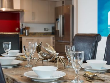 A dining table set with white bowls plates and glasses with metal crab decorations in a kitchen at Upper Deck in Rock