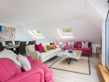 A living room with pink and beige sofas a wooden coffee table a dining table with black chairs and skylight windows at Upper Deck in Rock