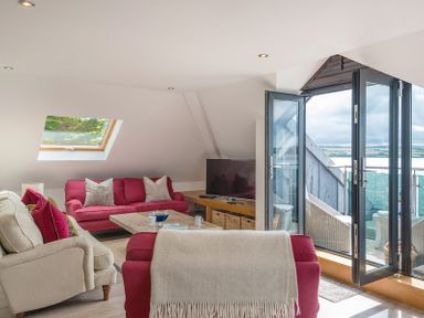 A living room with red and beige sofas a wooden coffee table and an open glass door leading to a balcony at Upper Deck in Rock