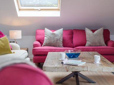 A living room with pink sofas a wooden coffee table with cups and a bowl under a skylight window at Upper Deck in Rock
