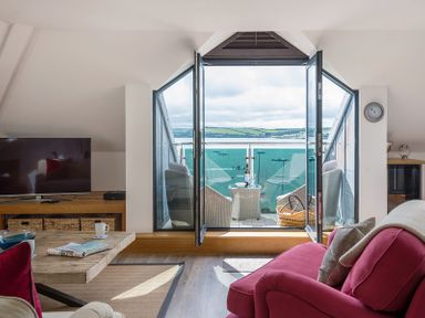 A living room with a red sofa a wooden coffee table a television and glass doors opening to a balcony with chairs overlooking water at Upper Deck in Rock