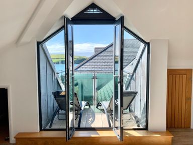 A balcony with two lounge chairs overlooking a roof and water through open double glass doors at Upper Deck in Rock