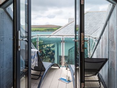 A balcony with two lounge chairs a towel and a cup on a tray overlooking water and hills at Upper Deck in Rock
