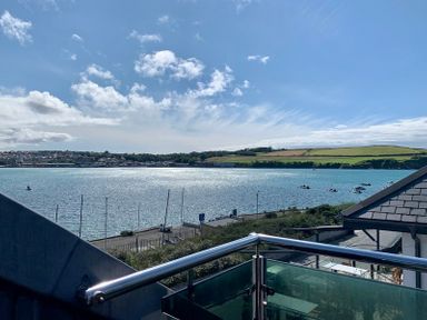 A balcony with metal railing overlooking a body of water with boats and distant hills at Upper Deck Rock