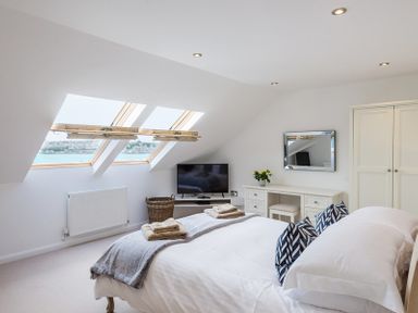 A bedroom with a bed, pillows, folded towels, slanted windows, a TV, a wicker basket, a dressing table with a mirror and flowers, and a wardrobe at Upper Deck Rock