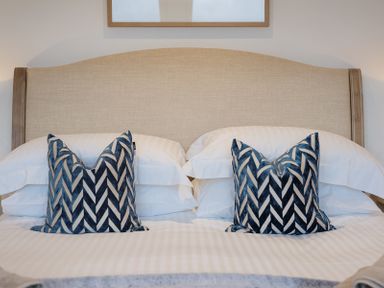 A bed with a beige headboard white pillows and two blue patterned decorative cushions at Upper Deck Rock