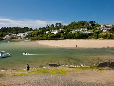 A beach with people walking near water and houses on a hill at Upper Deck in Rock