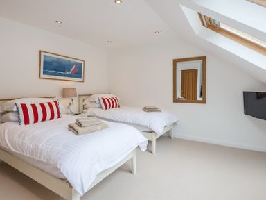 A bedroom with two single beds white bedding pillows with red stripes a lamp a wall mirror a wooden door and a skylight window at Upper Deck Rock