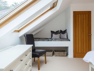 A room with a white dresser black chair built in seating with cushions and two baskets under a skylight at Upper Deck in Rock