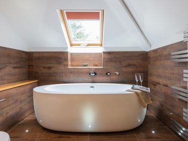 A bathroom with a white freestanding bathtub under a skylight window with brown tiled walls and floor at Upper Deck in Rock