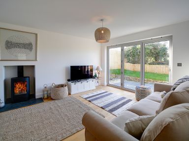A living room with a sofa a fireplace a television and sliding glass doors at Elmwood in Port Isaac