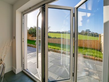 An open glass door leading to a patio and a fenced grassy area at Elmwood in Port Isaac