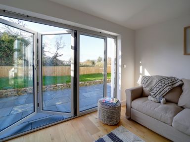 A living room with a beige sofa next to folding glass doors leading to a garden at Elmwood in Port Isaac