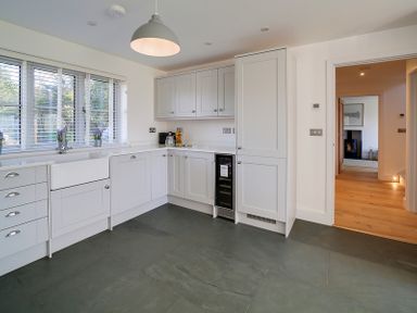 A kitchen with white cabinets a farmhouse sink and a window with blinds at Elmwood in Port Isaac