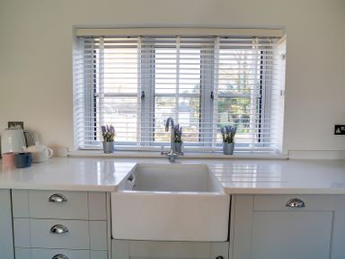 A kitchen sink under a window with white blinds and potted plants on the sill at Elmwood in Port Isaac