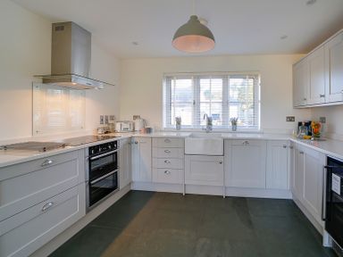 A kitchen with white cabinets a stove oven under a hood a sink under a window and small kitchen appliances on the countertop at Elmwood in Port Isaac