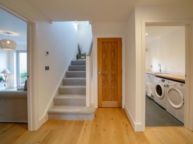 A hallway with carpeted stairs wooden door and laundry room with washing machine and dryer at Elmwood in Port Isaac