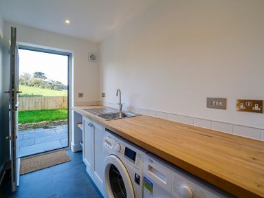 A utility room with a wooden countertop a sink washing machine and dryer with a door open to a garden at Elmwood in Port Isaac