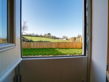 A partially open door showing a grass lawn and wooden fence with fields and houses in the background at Elmwood in Port Isaac