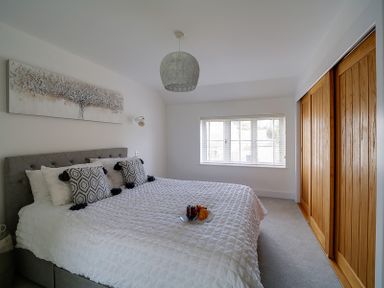 A bedroom with a bed with patterned pillows and white bedding a window with blinds and wooden sliding closet doors at Elmwood in Port Isaac