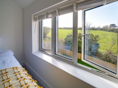 A bedroom window partially open with a view of a green field and trees at Elmwood in Port Isaac