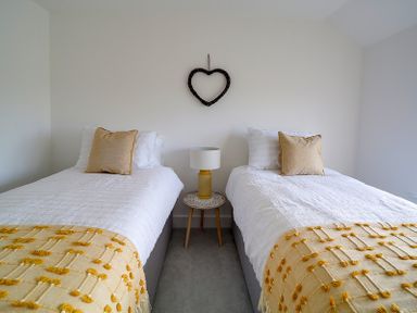 A bedroom with two single beds a bedside table and a heart-shaped wall decoration at Elmwood in Port Isaac