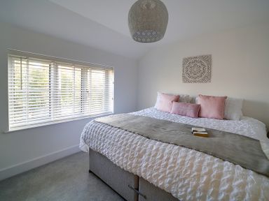 A bedroom with a large bed with pink pillows a window with blinds and a wall decoration at Elmwood in Port Isaac