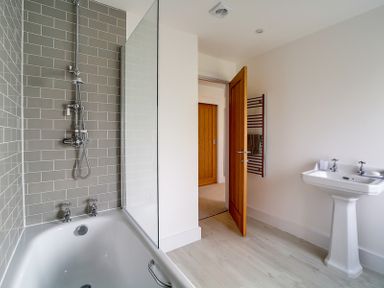 A bathroom with a bathtub shower combination a pedestal sink a wooden door and a towel rack at Elmwood in Port Isaac