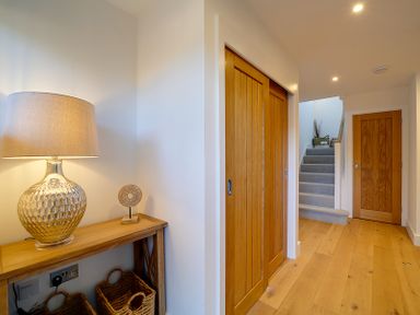 A hallway with wooden floors wooden doors a wooden console table with a lamp baskets and stairs at Elmwood in Port Isaac