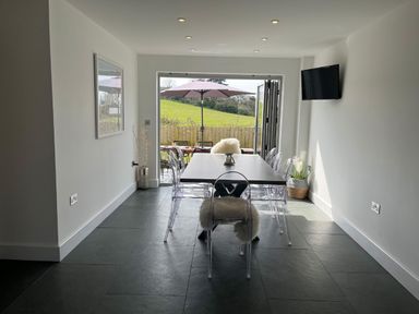 A dining area with a table and transparent chairs facing an open patio door with an umbrella outside at Elmwood in Port Isaac