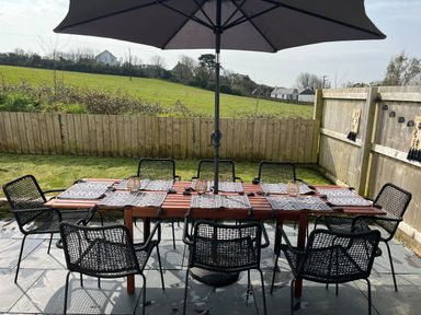 An outdoor patio dining area with a wooden table and eight black mesh chairs under a large black umbrella at Elmwood in Port Isaac