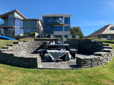 A stone patio with a picnic table and benches in front of modern houses at Egloskerry in New Polzeath