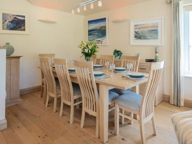 A dining room with a wooden table set for eight and paintings on the walls at Egloskerry in New Polzeath