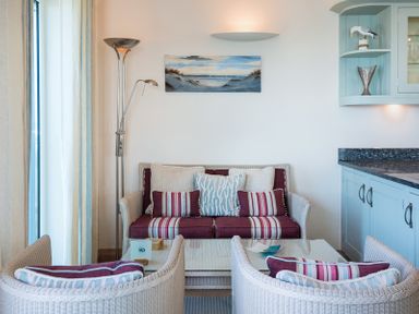 A sitting area with a sofa and two chairs with cushions and a glass coffee table at Egloskerry in New Polzeath