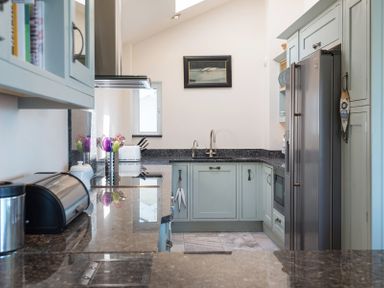 A kitchen with mint green cabinets black countertops stainless steel appliances and a sink at Egloskerry in New Polzeath