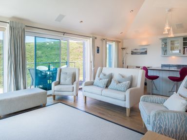 A living room with armchairs sofa ottoman and bar stools with a view of green hills at Egloskerry in New Polzeath