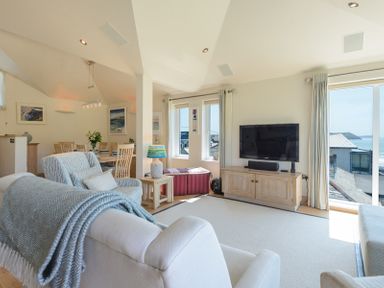 A living room with armchairs a wooden cabinet a television and a dining area with a table and chairs at Egloskerry in New Polzeath