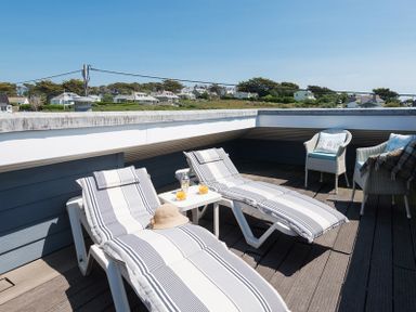 A rooftop terrace with two striped lounge chairs a small table with drinks and two wicker chairs at Egloskerry in New Polzeath