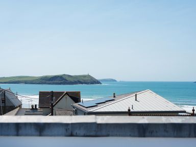 A view of rooftops with solar panels and a distant green island over the ocean at Egloskerry in New Polzeath
