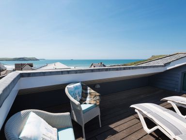 A rooftop terrace with chairs and loungers overlooking the ocean and rooftops at Egloskerry in New Polzeath